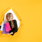 young-fashion-woman-with-shopping-bags-through-torn-paper-hole-wall